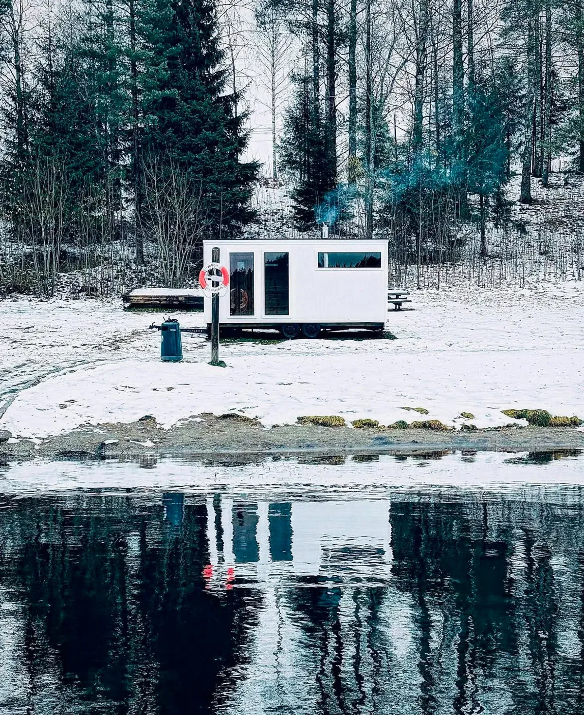 A mobile sauna wagon parked beside a snowy Norwegian lake in winter