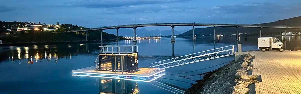 A person stepping into a cold Norwegian fjord from a sauna platform in winter