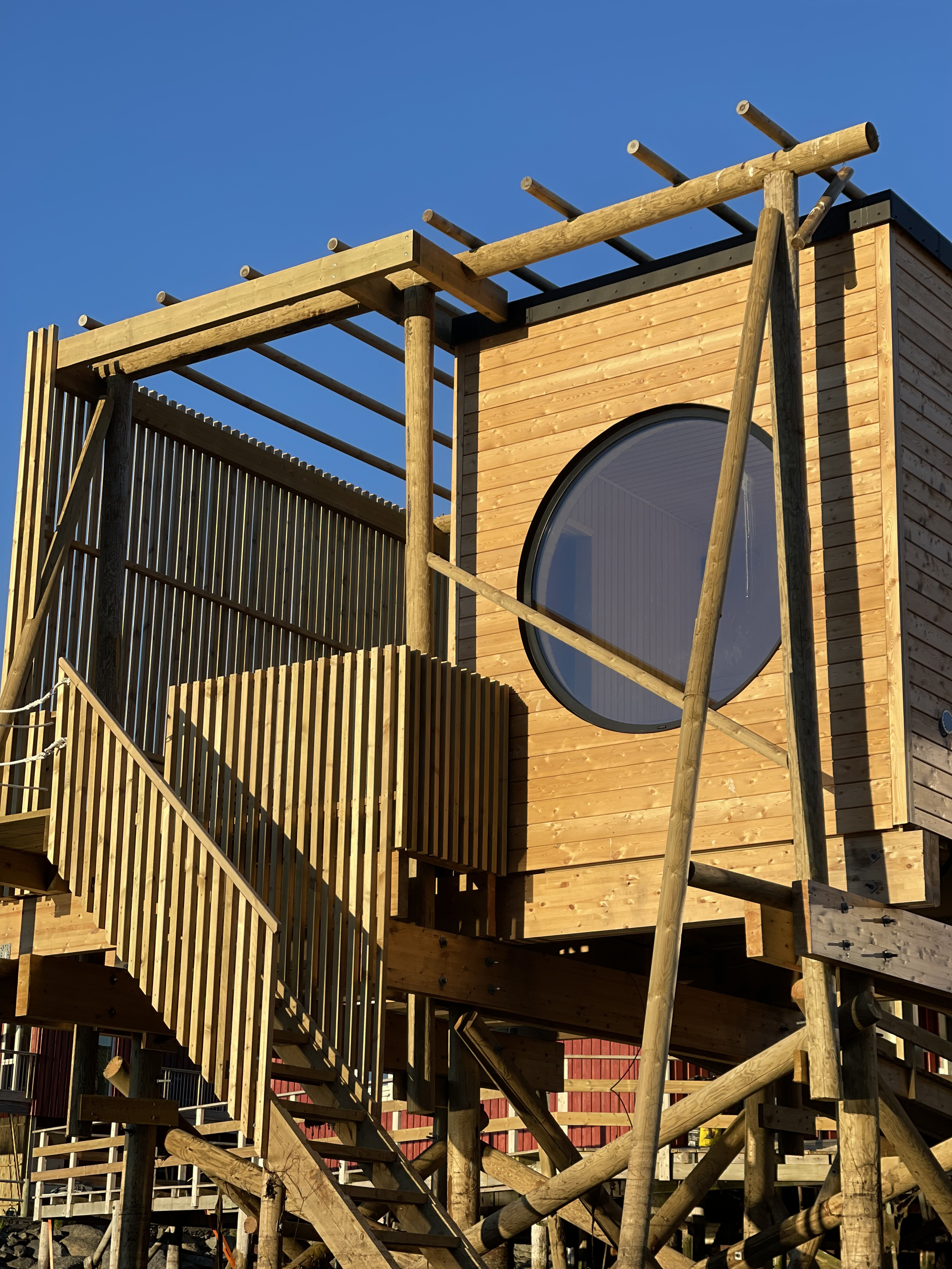 A wooden sauna cabin at Hemmingodden in Ballstad, Lofoten, with the harbour and mountain peaks behind