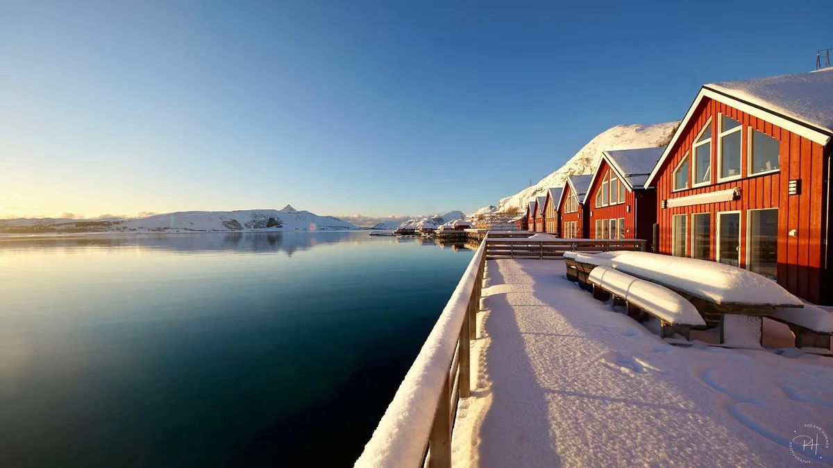 Wood-fired sauna cabin on the Lofoten shore with sharp granite peaks and midnight-sun light behind